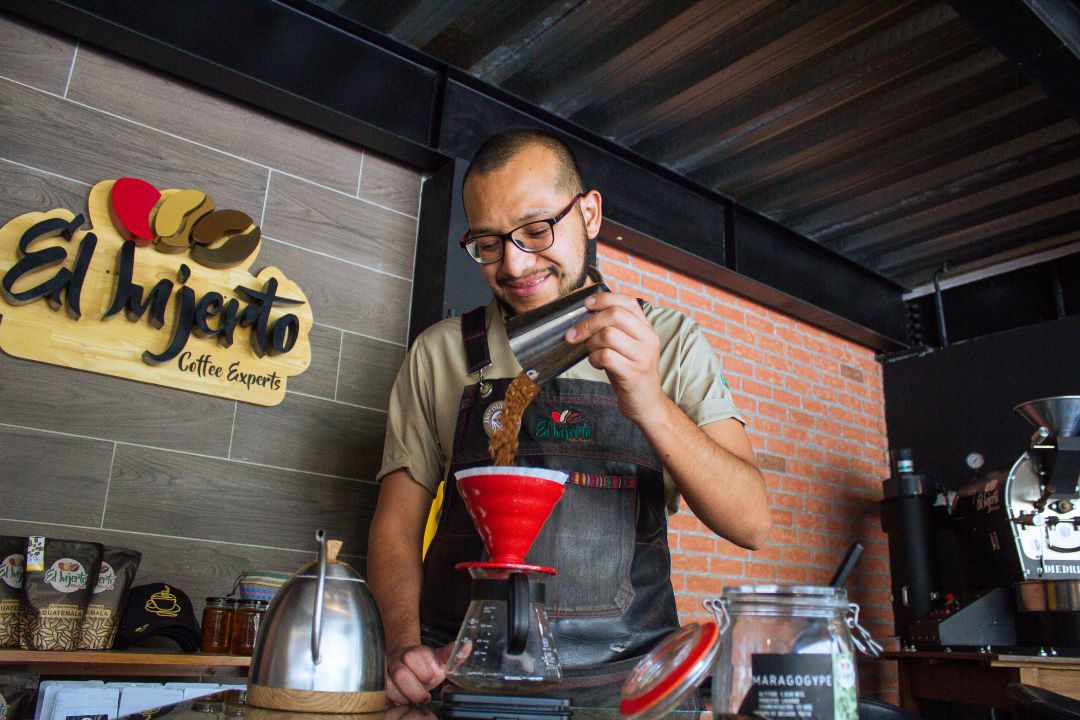 Un barista vertiendo granos de café Groud en una bandeja de goteo